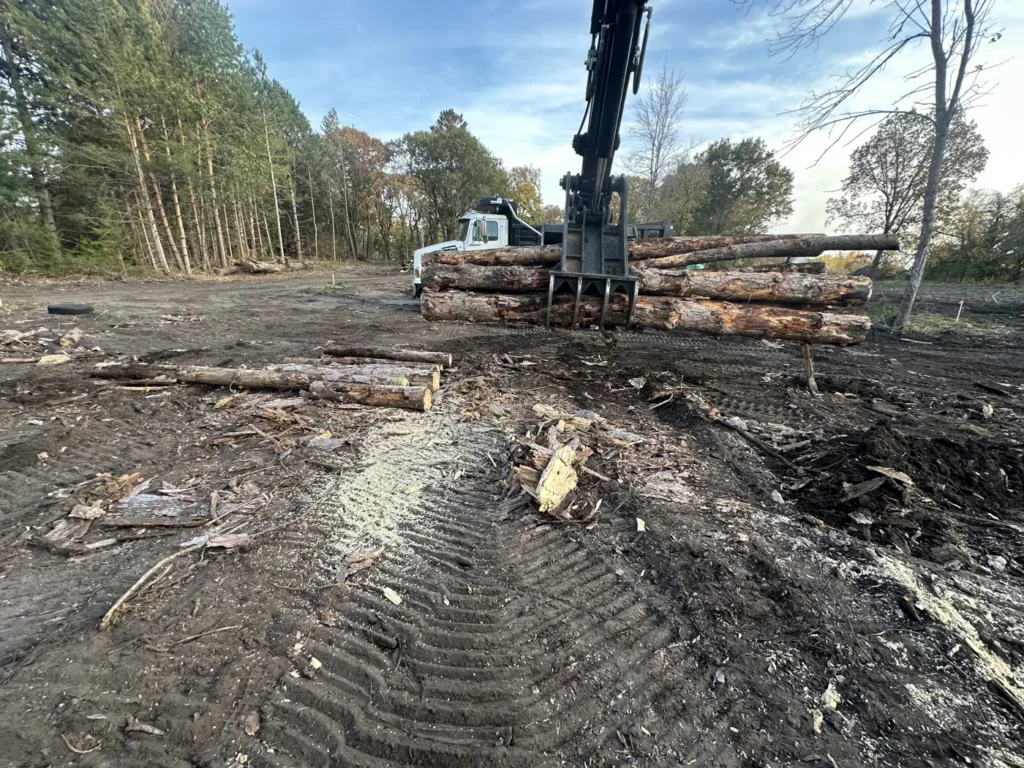 Excavator handling stacked timber on cleared ground
