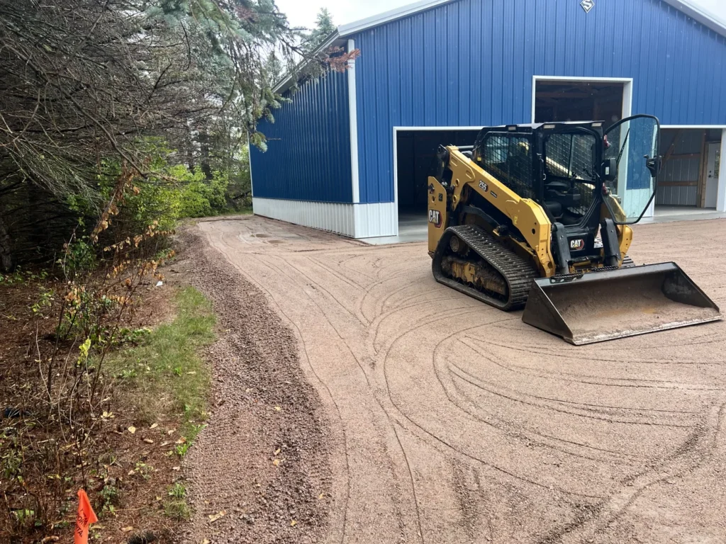 Compact tracked loader on a prepared gravel access beside a building