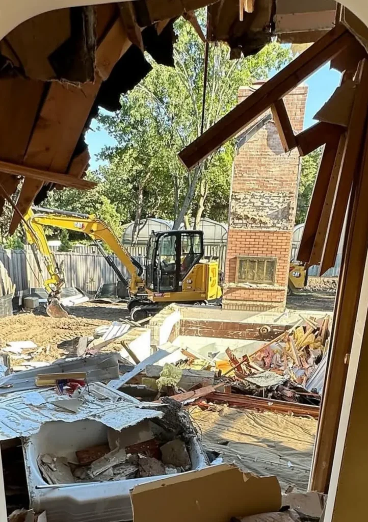 View through a partially removed structure toward an excavator and demolition materials