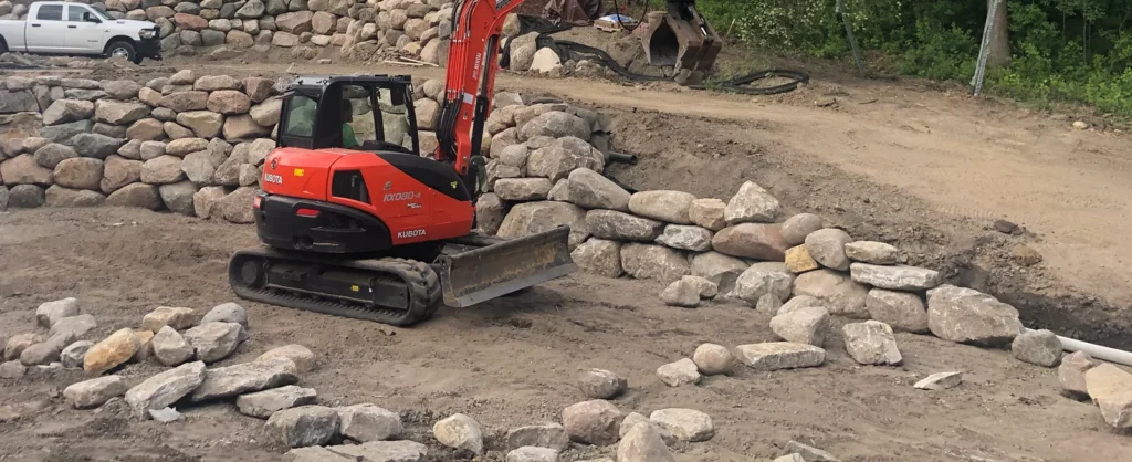 Compact excavator working beside tiered stone retaining walls